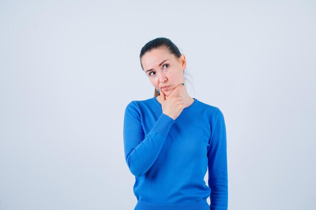 Jeune fille pense en tenant la main sur le menton sur fond blanc