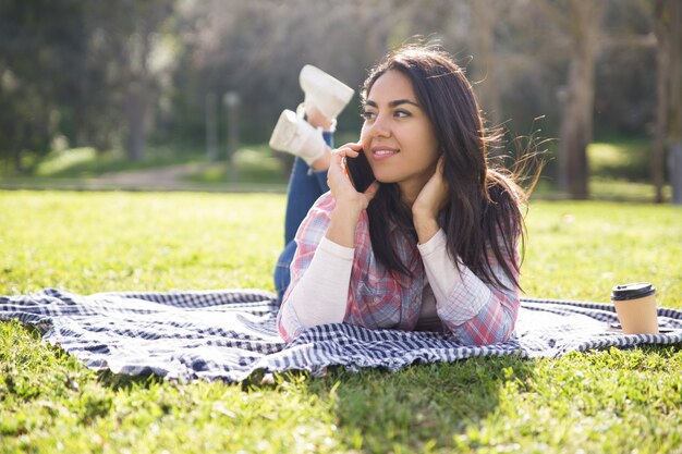 Jeune fille pensive souriante se reposant sur l&#39;herbe et parlant à la cellule