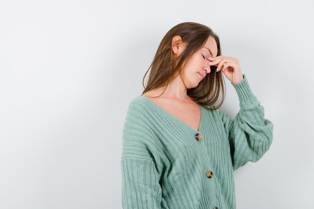 Jeune fille pinçant le pont du nez en maille et à l'ennui. vue de face.