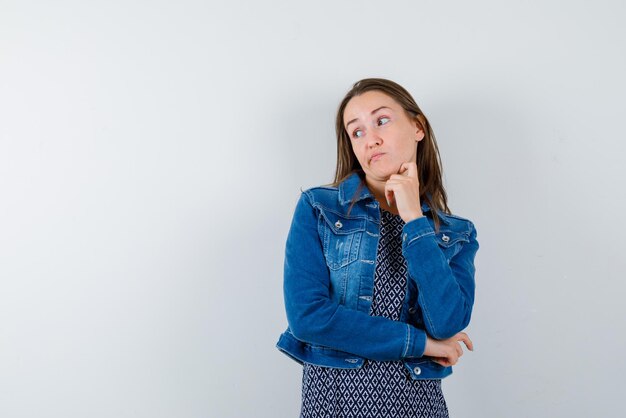 Jeune fille plissant ses lèvres et pensant à quelque chose en appuyant ses mains sur son menton sur fond blanc