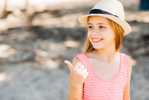 Jeune fille pointant loin avec le pouce sur la plage