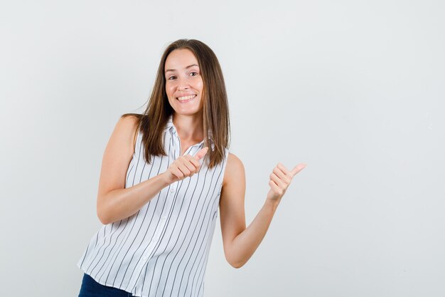 Jeune fille pointant les pouces en t-shirt, jeans et à la joyeuse vue de face.