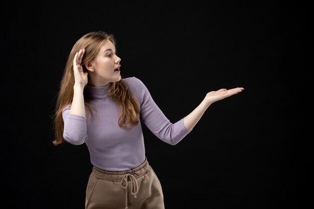 Jeune fille pointant quelque chose sur le côté gauche et écoutant attentivement dans l'obscurité