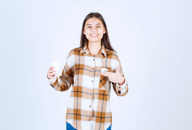 jeune fille pointant sur une tasse de thé sur un mur blanc.