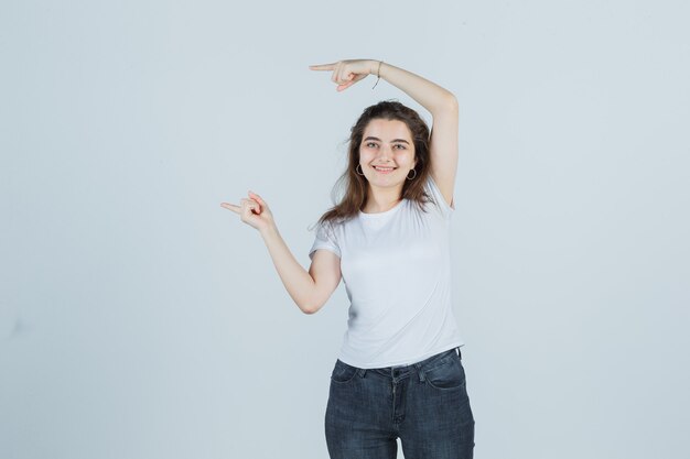 Jeune fille pointant vers le côté en t-shirt, jeans et à la recherche de plaisir. vue de face.