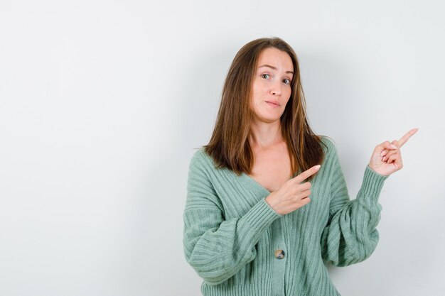 Jeune fille pointant vers la droite avec l'index en maille, jupe et à la grave, vue de face.