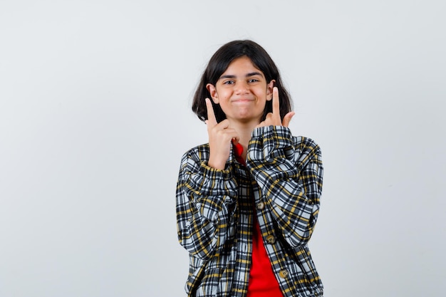 Jeune Fille Pointant Vers Le Haut En Chemise à Carreaux Et T-shirt Rouge Et L'air Heureux. Vue De Face.