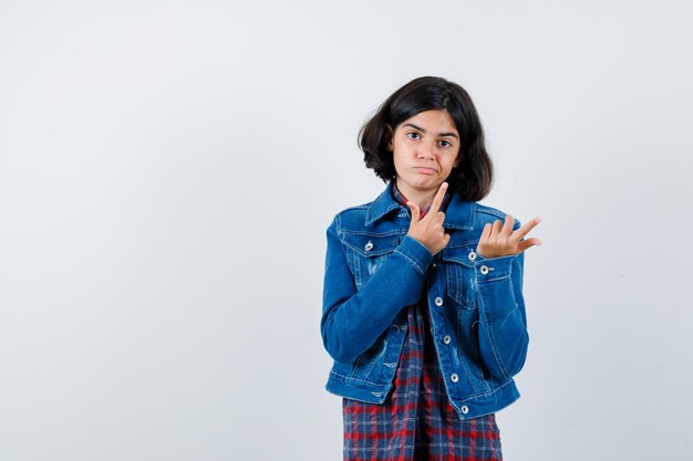 Jeune fille pointant vers le haut en chemise à carreaux et veste en jean et à la grave