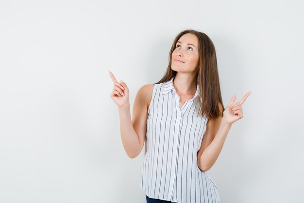 Jeune fille pointant vers le haut en t-shirt, jeans et à la recherche d'espoir. vue de face.