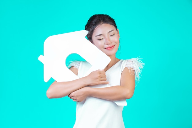 La jeune fille portait une chemise à manches longues blanche avec motif floral, tenant le symbole de la maison et montrant divers gestes en bleu.