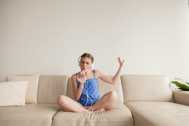 Jeune fille portant des écouteurs en écoutant de la musique sur un smartphone à la maison