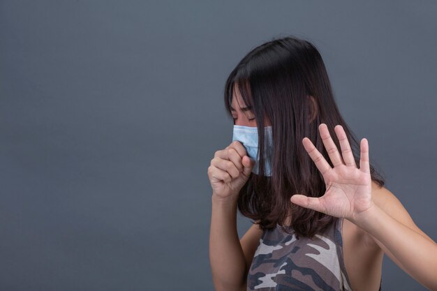 Jeune fille porte un masque en toussant sur le mur noir.