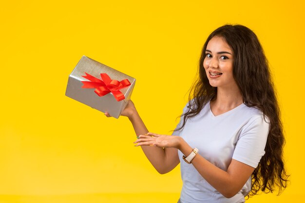 Jeune fille posant avec une boîte-cadeau dans la main et se sentir positif.