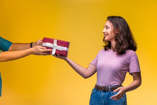 Jeune fille prenant un coffret cadeau de son amie à son anniversaire et a l'air heureuse.