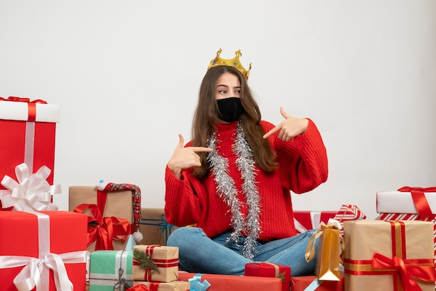 Jeune fille avec pull rouge assis autour de cadeaux avec masque noir sur blanc