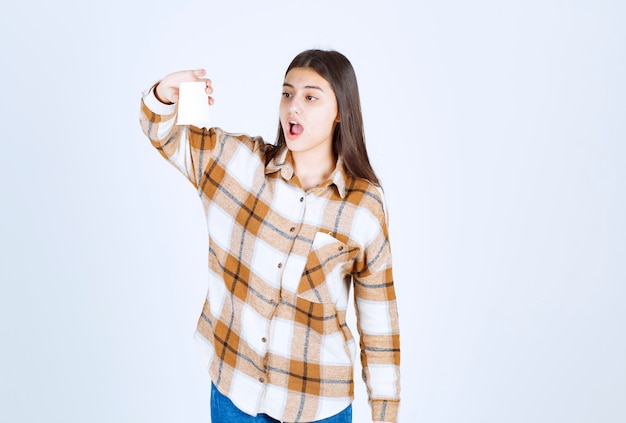 Photo gratuite jeune fille regardant une tasse vide sur un mur blanc.