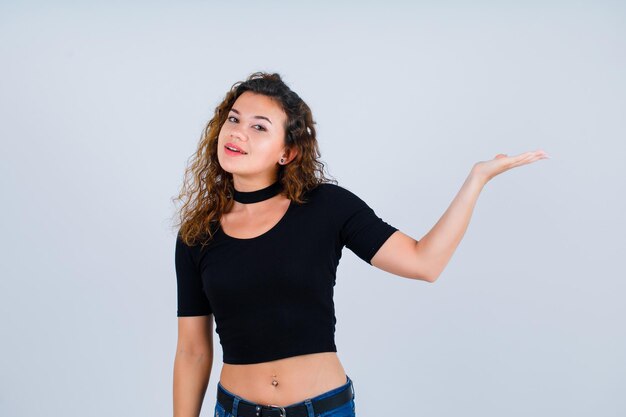 Jeune fille regarde la caméra en pointant vers la droite avec la main sur fond blanc