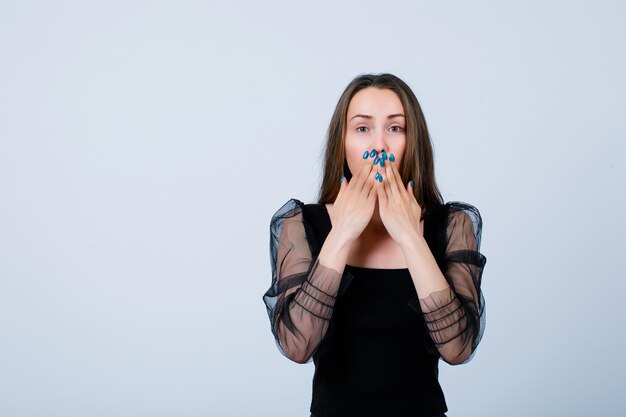 Jeune fille regarde la caméra en tenant les mains sur la bouche sur fond blanc