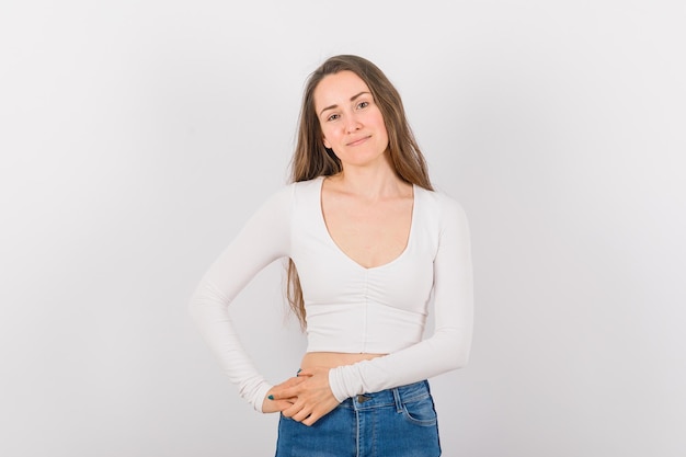 Jeune fille regarde la caméra en tenant les mains ensemble sur la taille sur fond blanc