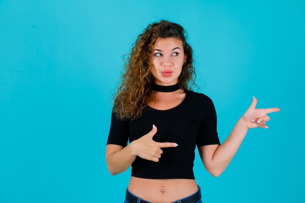 Jeune fille regarde à droite en pointant vers la droite avec les index sur fond bleu