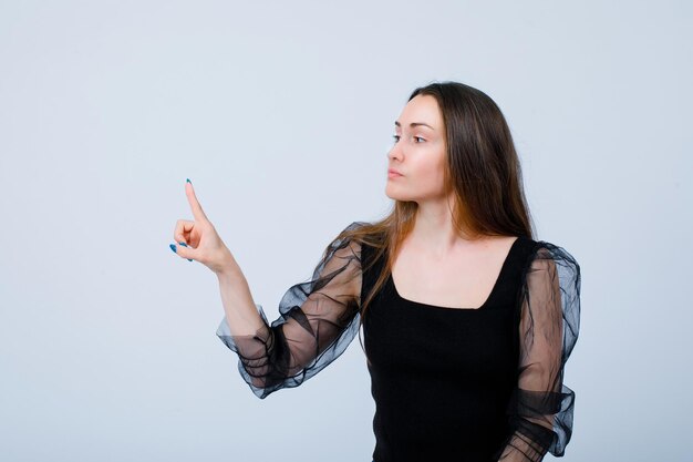 Jeune fille regarde à gauche et pointe là avec l'index sur fond blanc