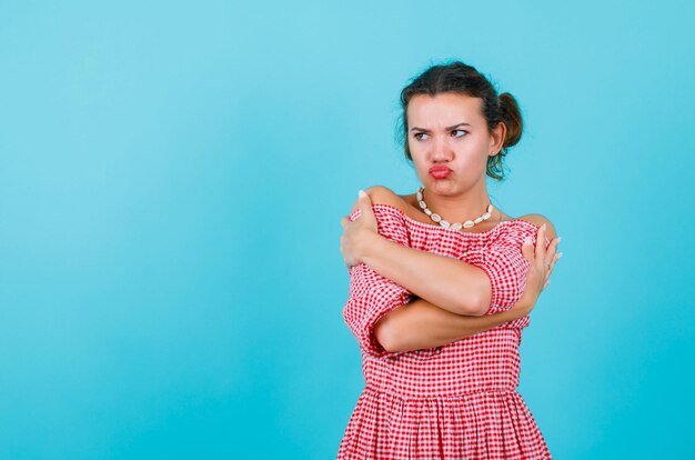 La jeune fille regarde loin en croisant les bras et en montrant un mimétisme triste sur fond bleu