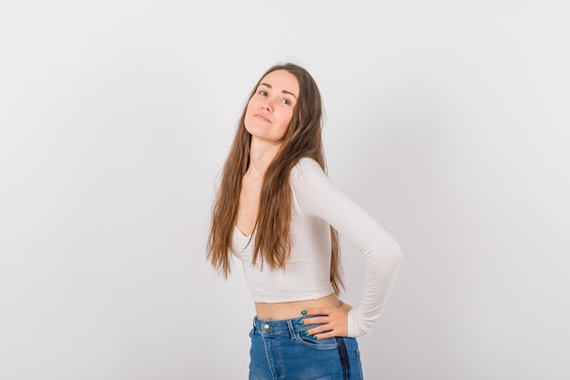 La jeune fille regarde loin en mettant la main sur la taille sur le fond blanc