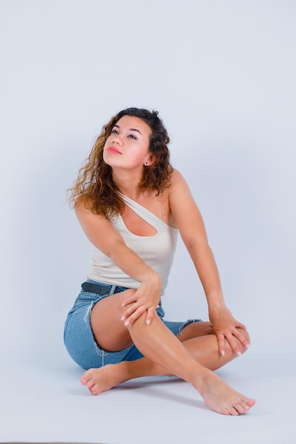 La jeune fille regarde loin en s'asseyant sur le plancher sur le fond blanc