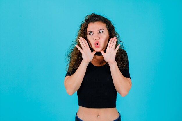 La jeune fille regarde loin en se tenant la main autour de la bouche sur fond bleu