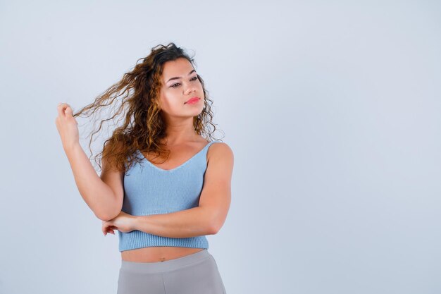 La jeune fille regarde loin en tenant des cheveux sur le fond blanc