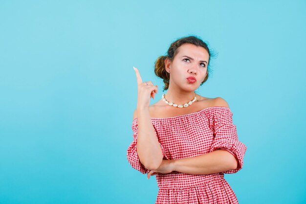 Jeune fille regarde et pointe vers le haut avec l'index sur fond bleu