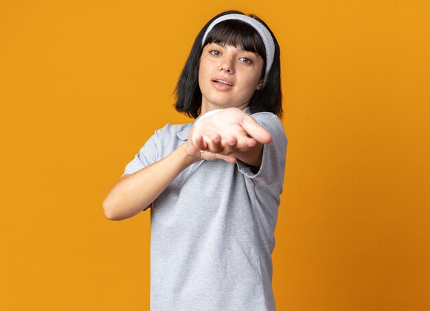 Jeune fille de remise en forme heureuse et confiante portant un bandeau étirant ses mains prêtes pour l'entraînement debout sur orange