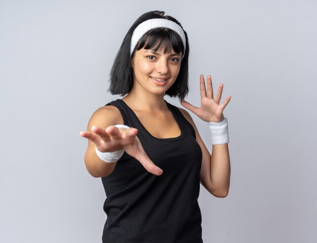 Jeune fille de remise en forme portant un bandeau regardant la caméra faisant des gestes avec les mains souriant joyeusement debout sur fond blanc