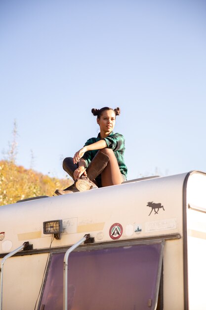 Jeune fille reposante sur le toit d'un camping-car rétro. Aventure dans la nature