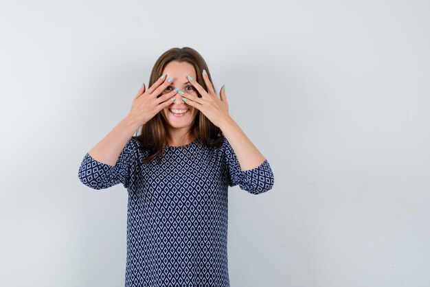 Jeune fille riant et tenant ses yeux entre ses doigts sur fond blanc