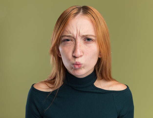 Jeune fille rousse au gingembre insatisfaite avec des taches de rousseur regardant la caméra sur vert olive