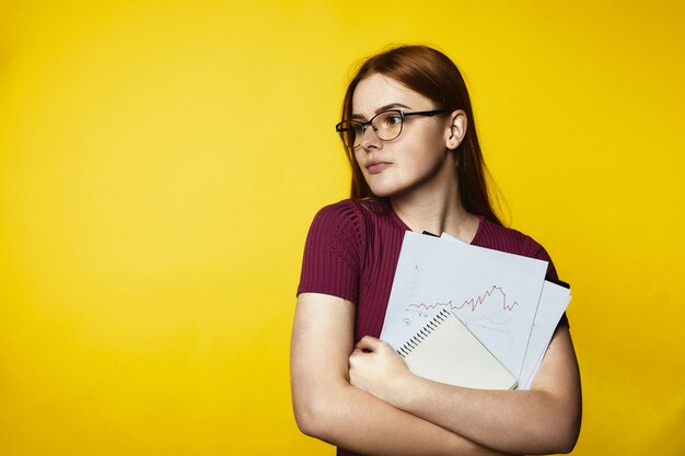 Jeune fille rousse portant des lunettes et tenant des graphiques et des documents