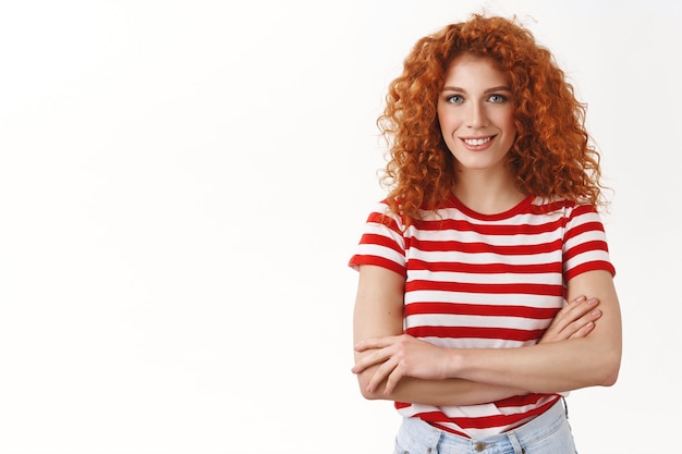 Photo gratuite jeune fille rousse séduisante et sûre d'elle, enthousiaste et bouclée, démarrant un nouveau projet, se sentant déterminée, encouragée par le succès, les bras croisés