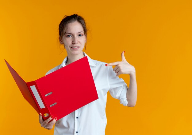 Jeune fille russe blonde agacée tient et pointe sur le dossier de fichiers sur orange avec copie espace