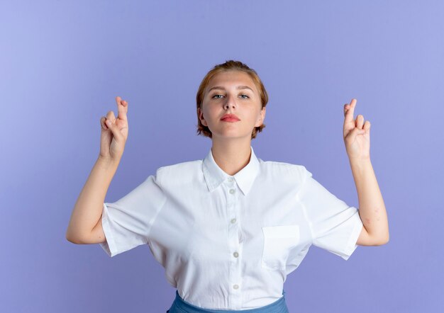 Jeune fille russe blonde confiante croise les doigts isolés sur fond violet avec copie espace