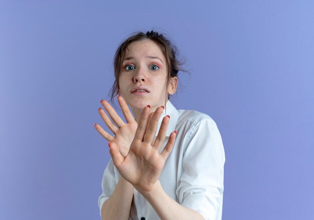 Jeune fille russe blonde effrayée défend avec les mains isolées sur l'espace violet avec copie espace