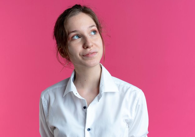 Jeune fille russe blonde heureuse regarde sur le côté rose avec copie espace