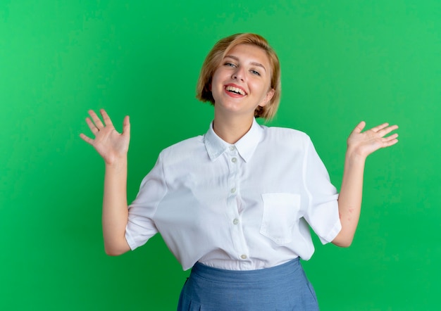 Jeune fille russe blonde joyeuse se tient avec les mains levées isolé sur fond vert avec copie espace