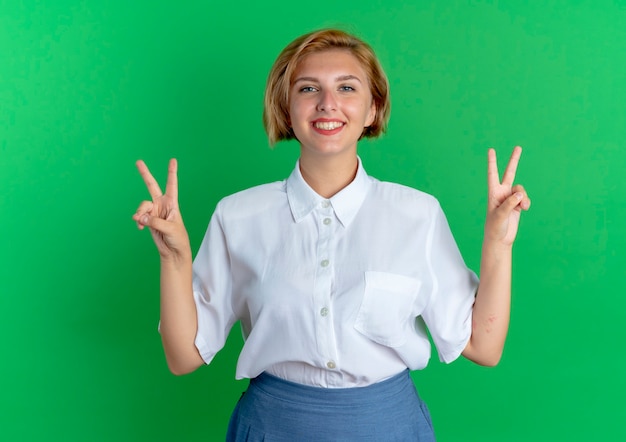 Jeune fille russe blonde souriante gestes signe de la main de la victoire avec deux mains isolé sur fond vert avec espace de copie