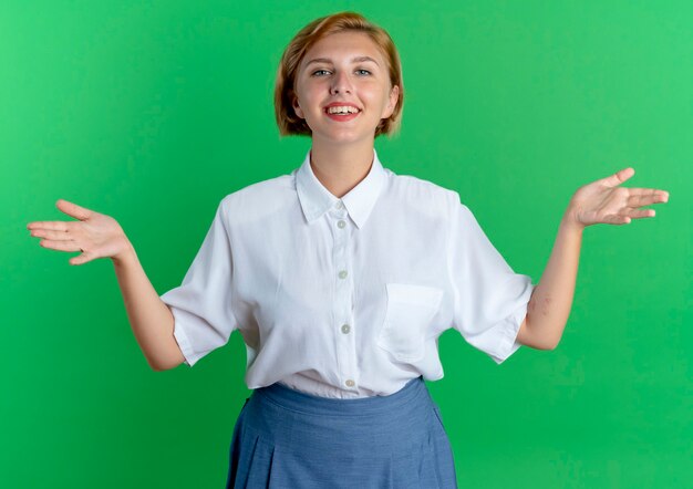 Jeune fille russe blonde souriante se tient avec les mains ouvertes isolé sur fond vert avec espace copie