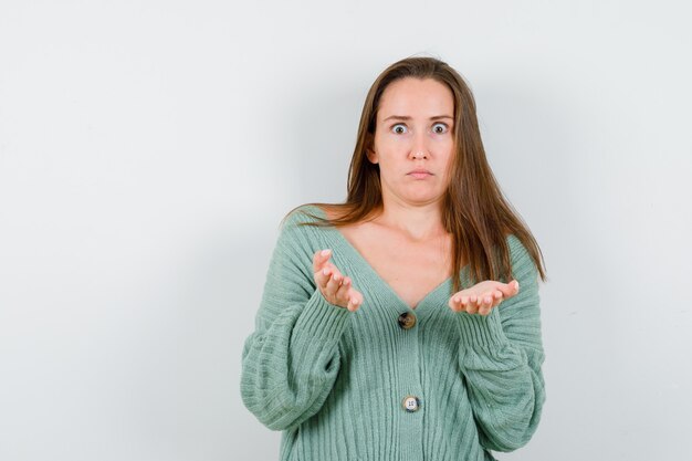 Jeune fille s'étendant les mains de manière interrogative en maille et à la déroute. vue de face.