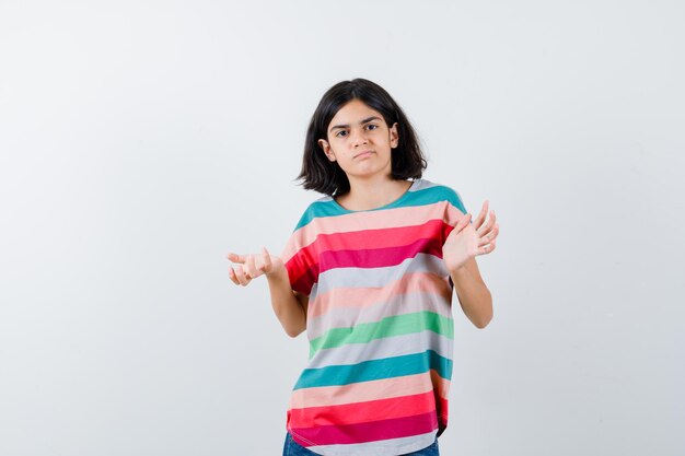 Jeune fille s'étirant les mains de manière interrogative en t-shirt à rayures colorées et à la perplexité. vue de face.