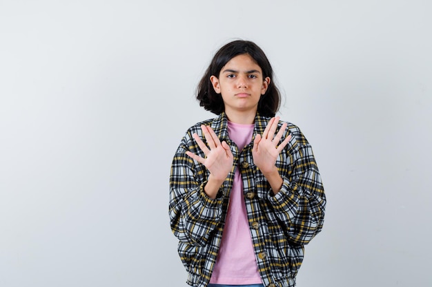 Jeune fille s'étirant les mains pour s'arrêter en chemise à carreaux et t-shirt rose et l'air sérieux. vue de face.