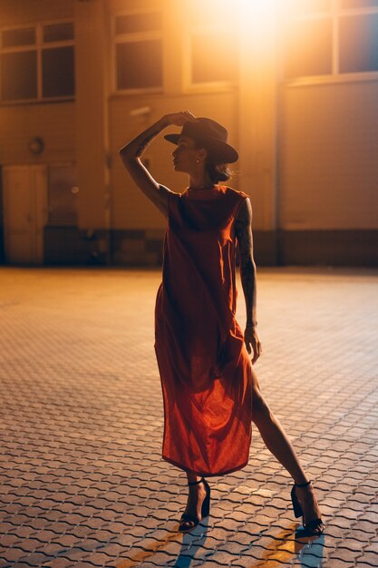 La jeune fille séduisante dans un chapeau pose à la caméra la nuit