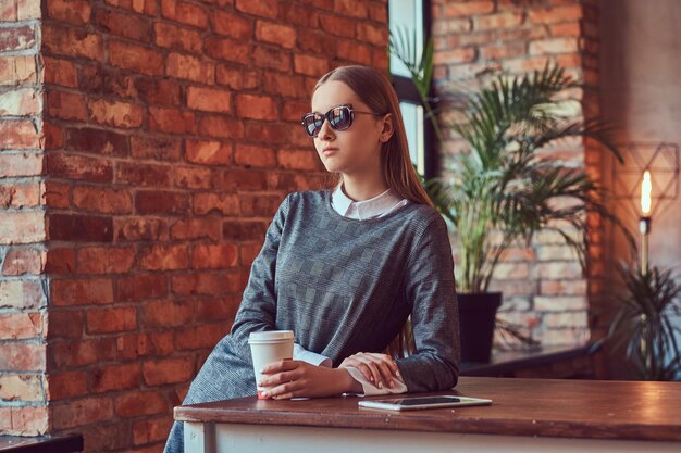 Une jeune fille sensuelle mince vêtue d'une robe grise et de lunettes de soleil penchées